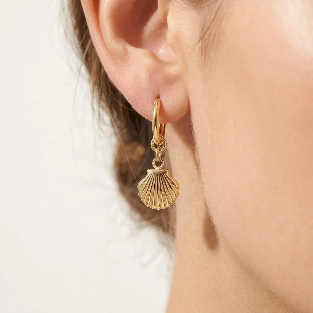 18K gold shell pendant huggie earrings by Winks Design Studio,LLC featuring delicate shell charms on small hoop earrings.