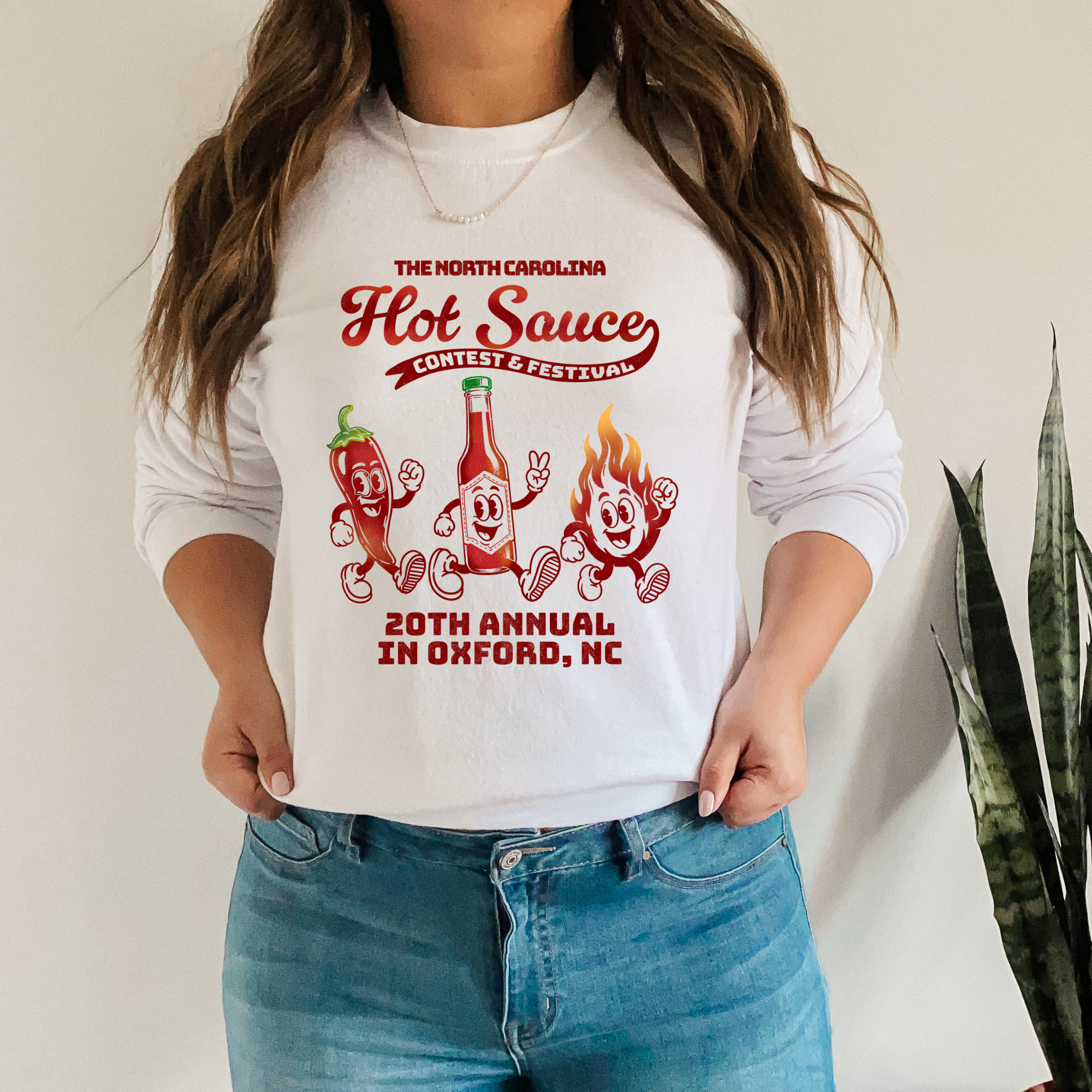 Long sleeve NC Hot Sauce Festival T-shirt featuring retro character design in bold colors, worn by a person.