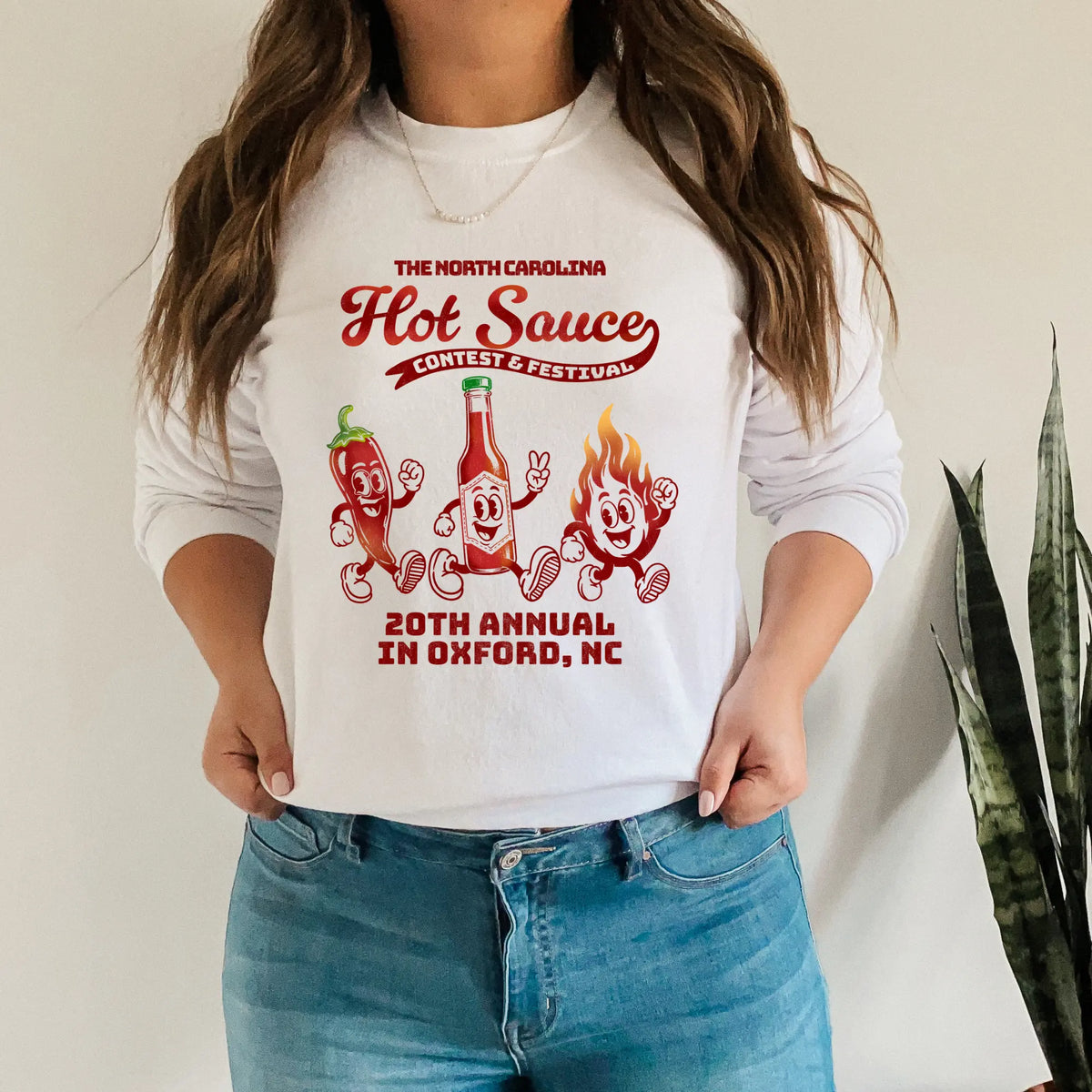 Long sleeve NC Hot Sauce Festival T-shirt featuring retro character design in bold colors, worn by a person.