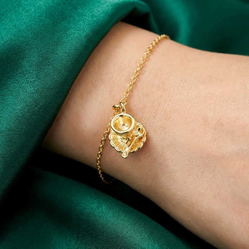 Gold teacup charm from Winks Design Studio, LLC, featuring a detailed miniature teacup with a shiny gold finish.