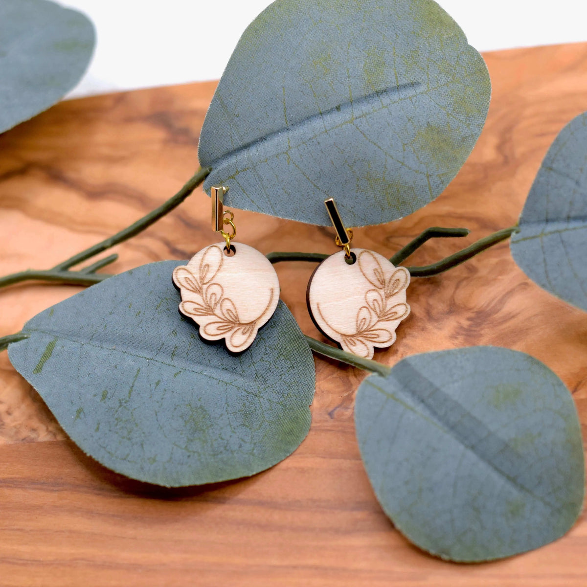 Wooden engraved eucalyptus earrings by Winks Design Studio, LLC, featuring natural wood texture and intricate engraved leaf design.