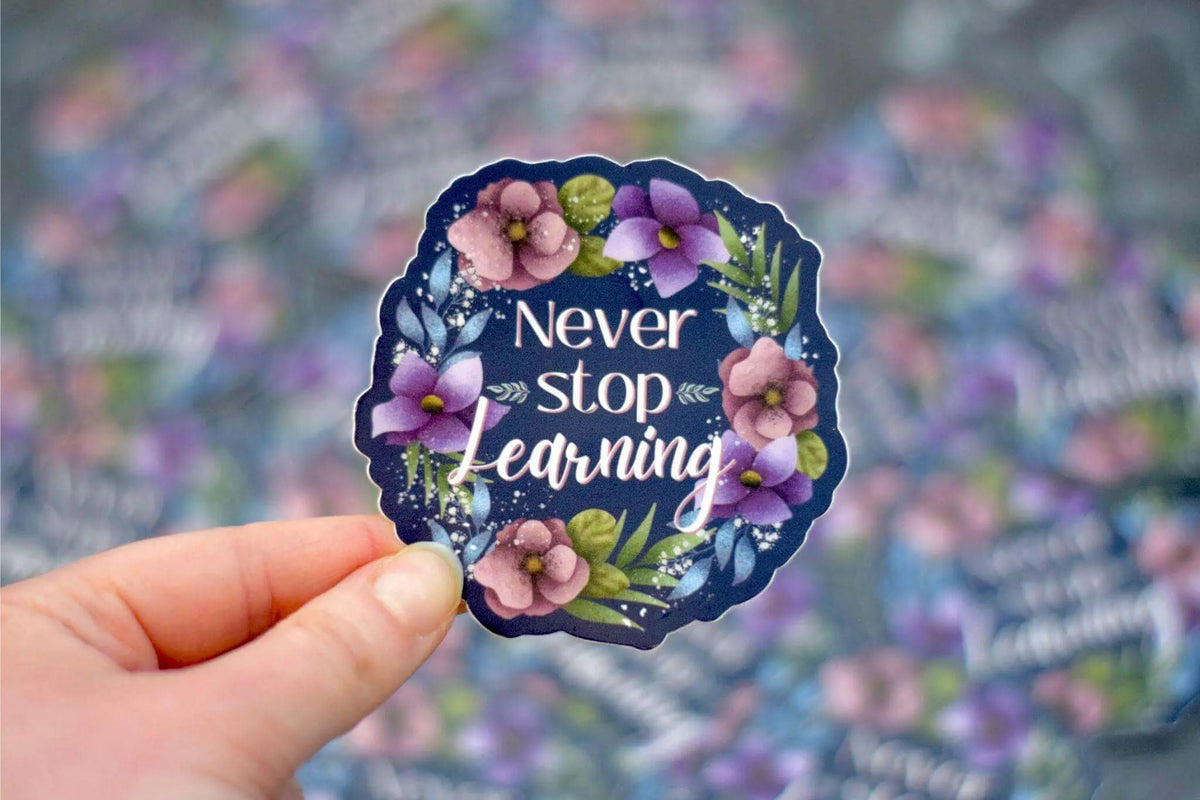 Vinyl sticker featuring "Never Stop Learning" text by Winks Design Studio, LLC, measuring 2x2 inches, with vibrant design.