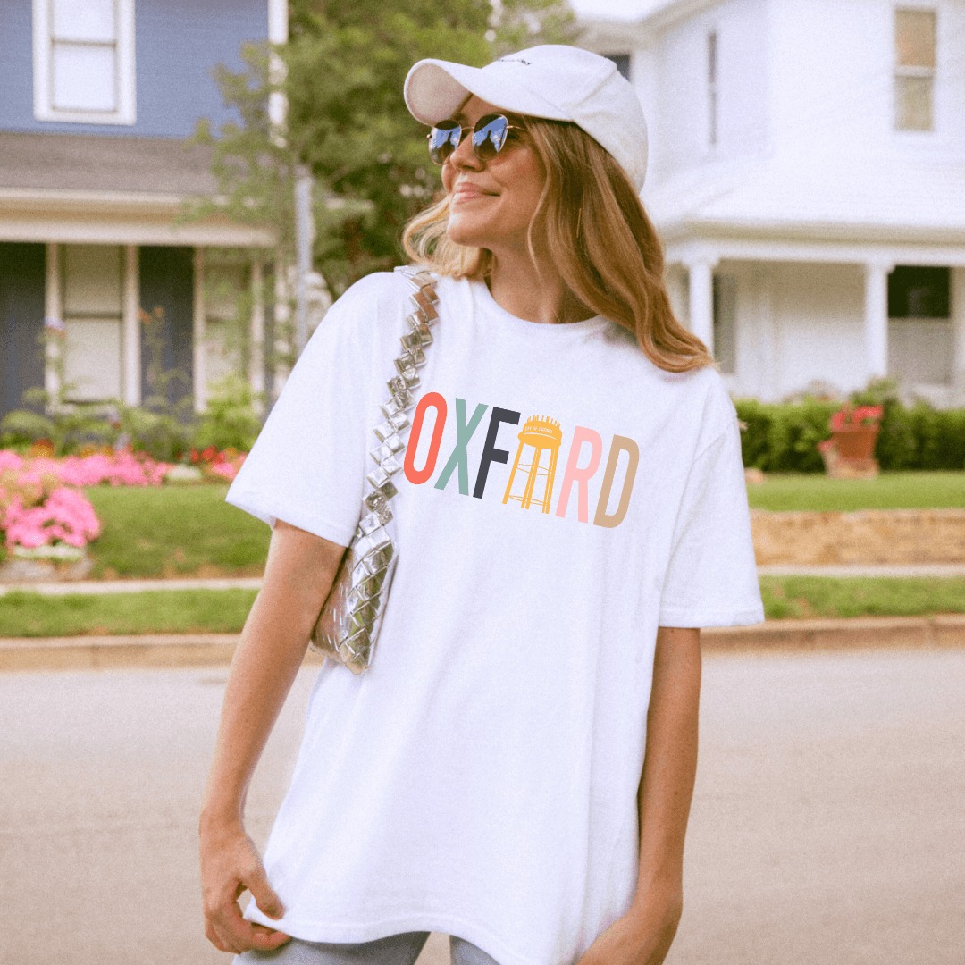 Woman wearing Color Blocked Oxford Water Tower T-shirt, showcasing hometown pride with vibrant multicolored design in a neighborhood setting.