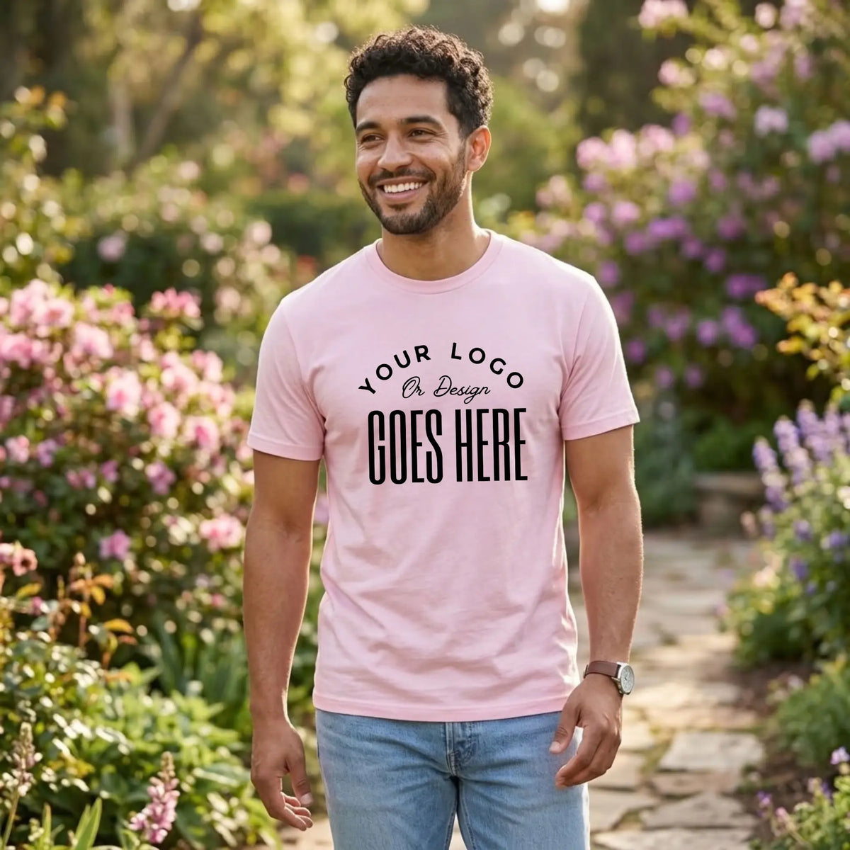 Man in a light pink custom t-shirt with a large black "Your Logo or Design Goes Here" center chest placeholder in a flower garden