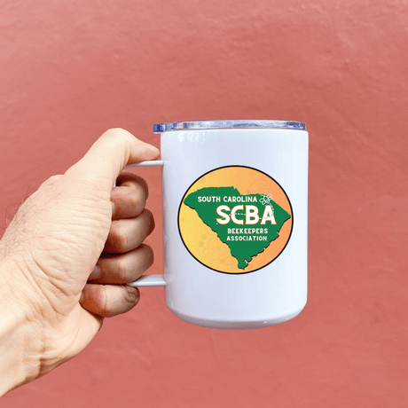 Hand holding SCBA 13 oz metal mug with South Carolina Beekeeper Association logo, perfect for hot and cold beverages.