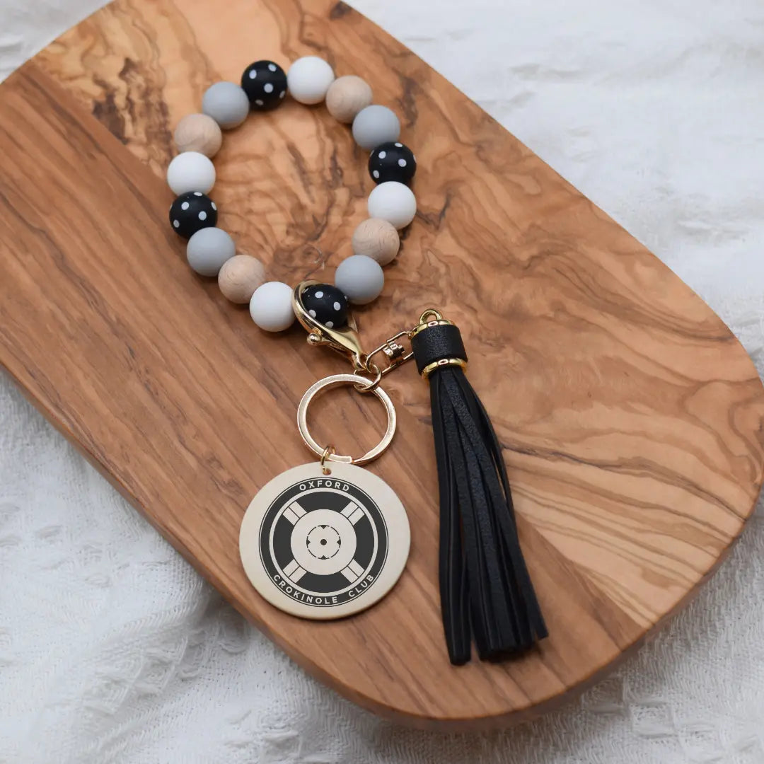 Engraved Oxford Crokinole Club wristlet keychain by Winks Design Studio, LLC featuring a leather strap and engraved club logo.