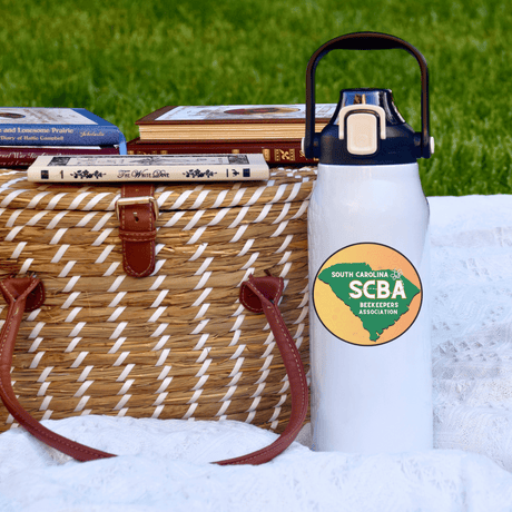 SCBA 57oz Water Bottle beside picnic basket on grass promoting South Carolina Beekeeper Association