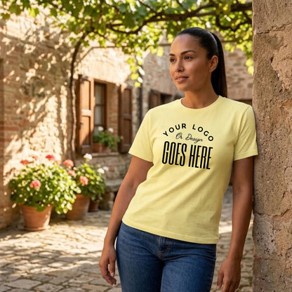 Woman in a pale yellow custom t-shirt with a large black "Your Logo or Design Goes Here" center chest placeholder in a stone courtyard