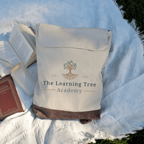 The Learning Tree Academy Rucksack Backpack on a blanket with books, showcasing logo and stylish design for students and professionals.