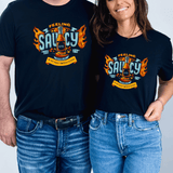 Two people wearing NC Hot Sauce Contest & Festival T-shirts with "Feeling Saucy" design and fiery graphics.