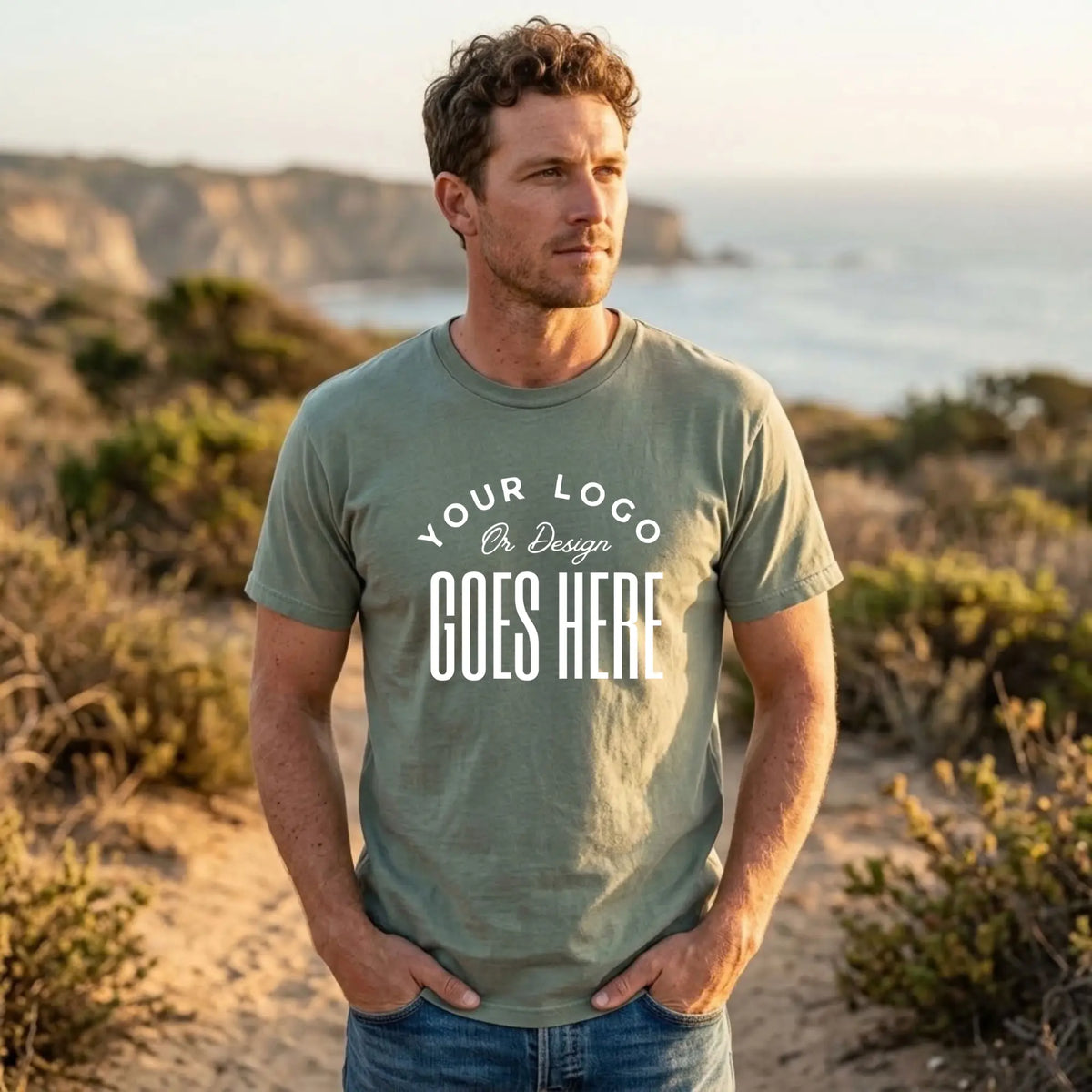 Sage green custom t-shirt with a large white "Your Logo or Design Goes Here" center chest placeholder print
