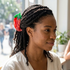 A woman with dark braided hair wearing a red and green strawberry-shaped hair clip, photographed in a softly blurred indoor setting.