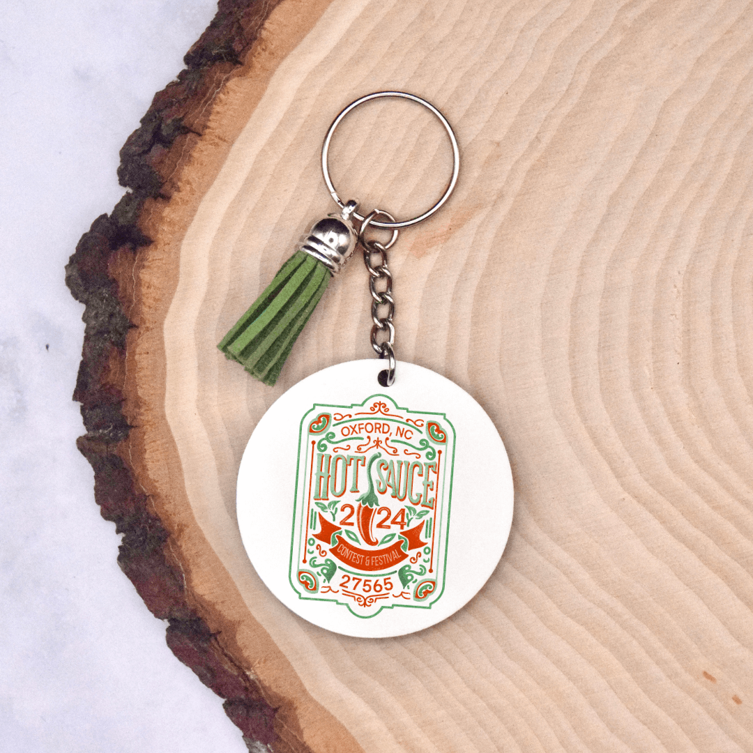 NC Hot Sauce Contest & Festival 2024 keychain with vintage label design and green tassel on wood background.