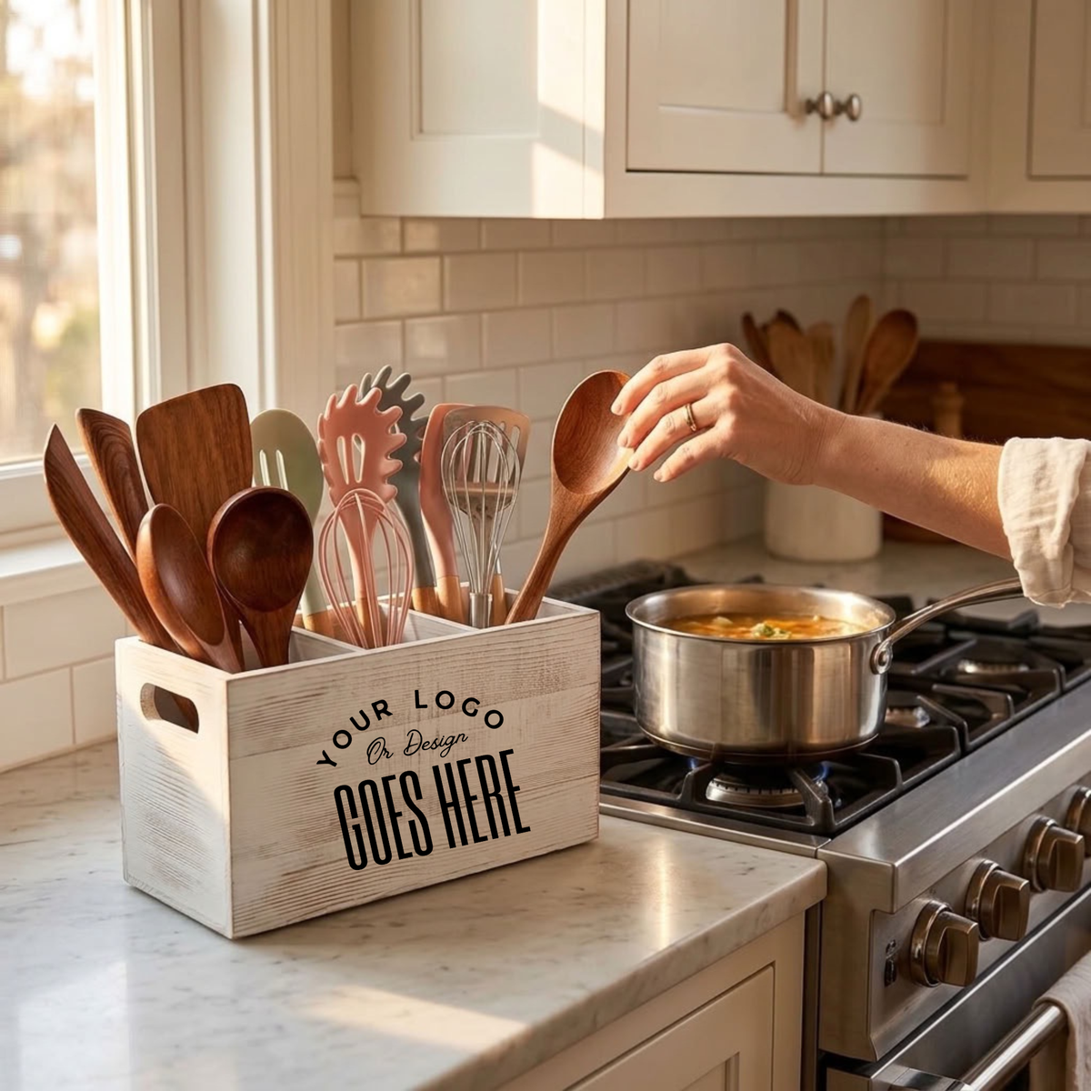 A personalized wooden kitchen utensil organizer box on a marble countertop in a bright kitchen. The box is light wood with black printed placeholder text reading &