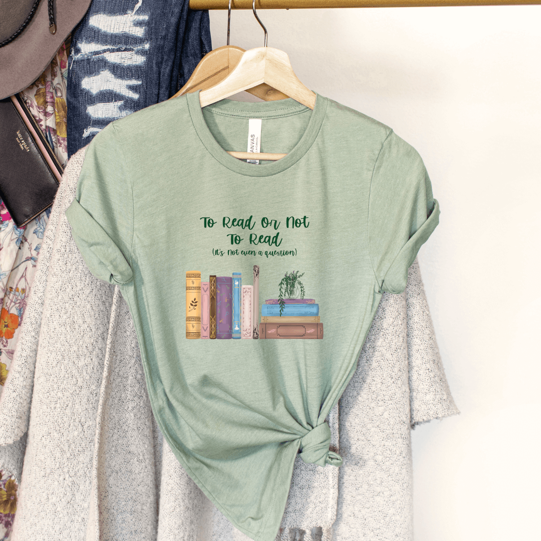 Green To Read Or Not To Read T-Shirt with whimsical book stack design hanging on clothes rack, showcasing literary passion.