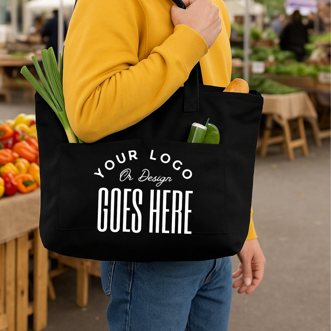 Person holding a black tote bag with customizable text at an outdoor market.