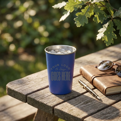 A blue insulated travel tumbler with a stainless steel rim sits on a wooden picnic table outdoors. The tumbler has placeholder text reading &