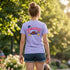 A woman viewed from behind wearing a light lavender-purple t-shirt with a colorful &