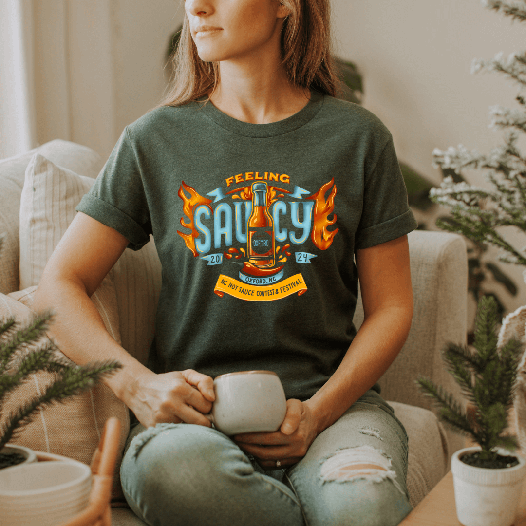 "Woman wearing NC Hot Sauce Festival T-shirt with Feeling Saucy design while relaxing with a cup of coffee"