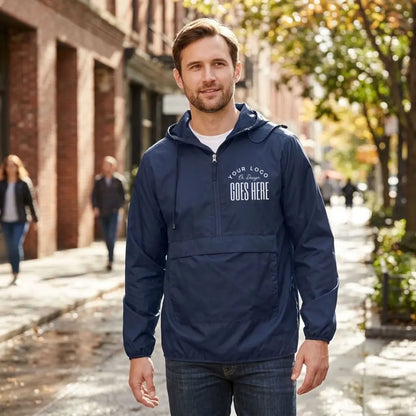 Man in a navy custom quarter zip windbreaker with a white "Your Logo or Design Goes Here" left chest placeholder on a city street