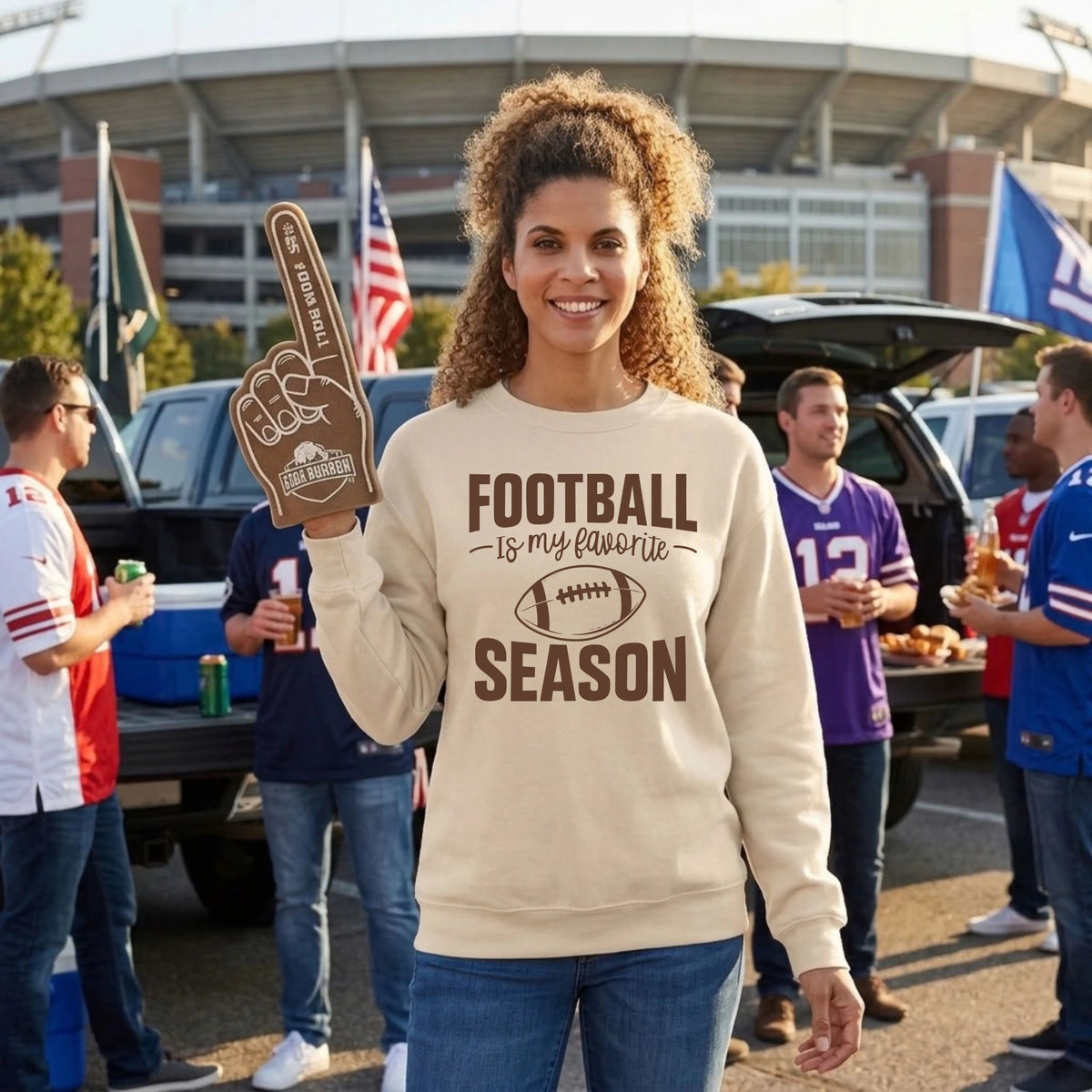 Smiling woman in a sand "Football Is My Favorite Season" graphic crewneck sweatshirt at a stadium tailgate