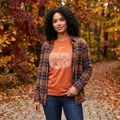 Woman in a heather autumn orange floral pumpkin graphic tee layered under a plaid flannel on a leafy fall path