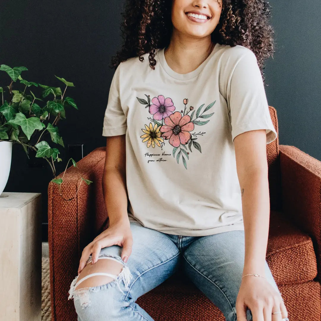 Winks Design Studio Happiness Blooms From Within T-shirt featuring a colorful floral design and inspirational text on soft fabric.