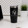 A black thermos cup with the MS Associates logo on it, placed on a white desk next to a laptop and a potted plant.