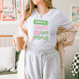 Woman wearing Kinda A Mess But Trying My Best T-Shirt, holding iced coffee, standing in cozy room.