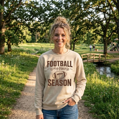 Smiling woman in a sand "Football Is My Favorite Season" graphic crewneck sweatshirt on a sunny park trail