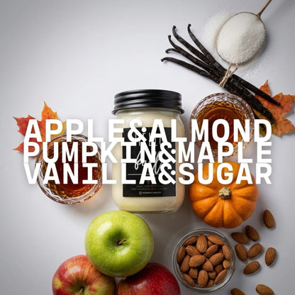 A candle in a clear glass jar with a black lid is centered on a light gray background, surrounded by autumn and almond ingredients including vanilla beans, sugar, apples, almonds, and a small pumpkin. Large white text across the center reads &