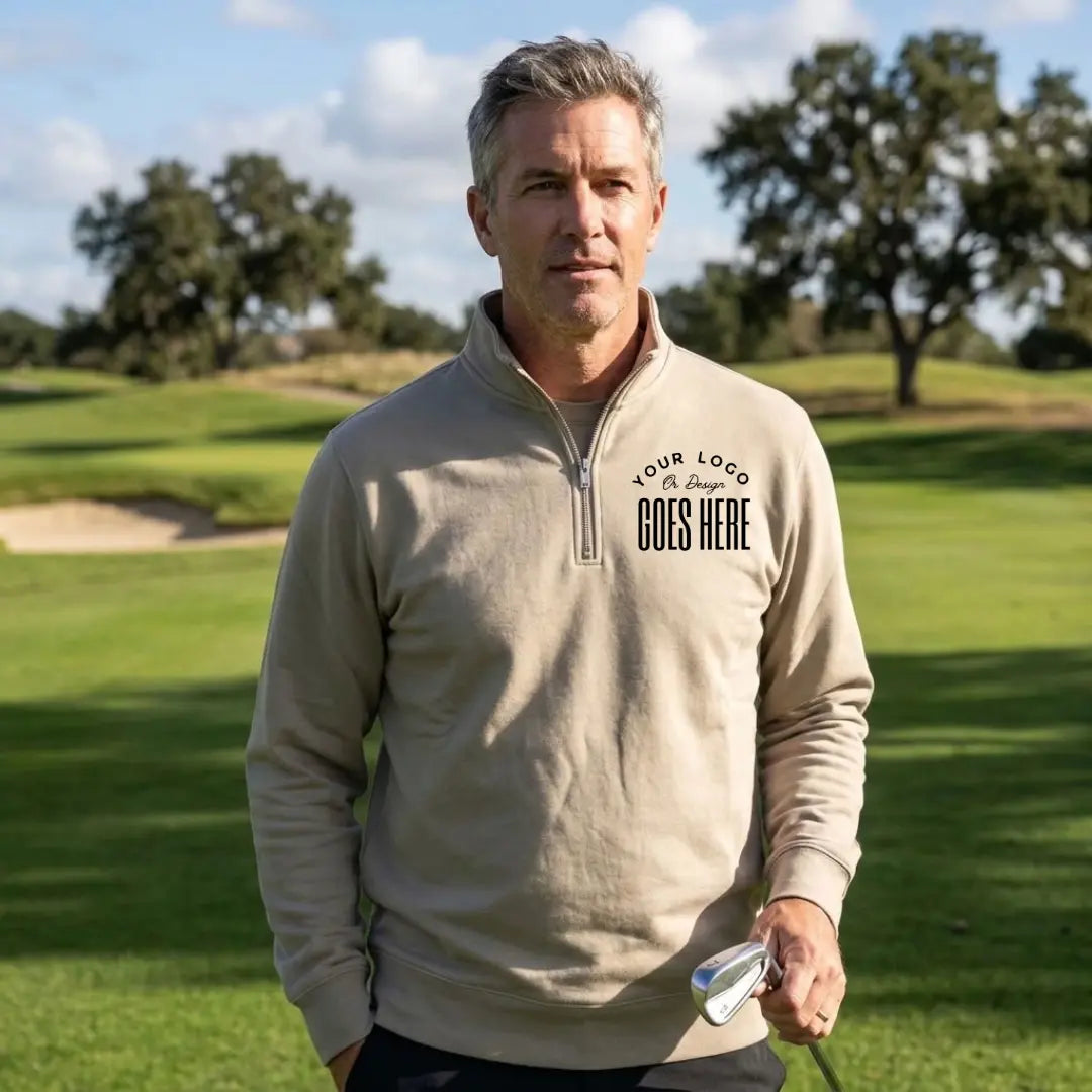 Man holding a golf club in a stone gray custom quarter zip sweatshirt with a black "Your Logo or Design Goes Here" left chest placeholder