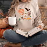 Woman wearing Pumpkin Patch Fall-Themed Crewneck holding a mug and reading a book by a fireplace with pumpkins.