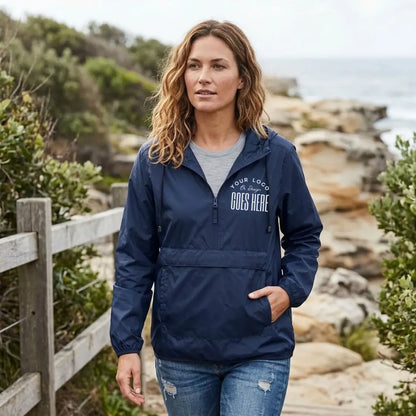 Woman in a navy custom quarter zip windbreaker with a white "Your Logo or Design Goes Here" left chest placeholder on a coastal path