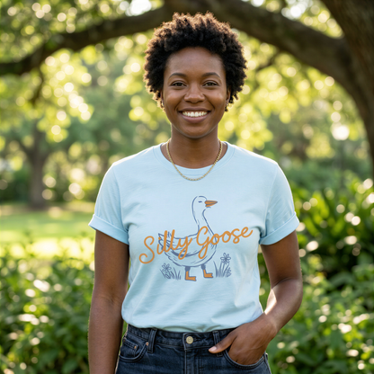 A smiling woman wearing a light blue t-shirt with a graphic of a goose and the text "Silly Goose" stands in a park surrounded by greenery.