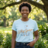 A smiling woman wearing a light blue t-shirt with a graphic of a goose and the text "Silly Goose" stands in a park surrounded by greenery.