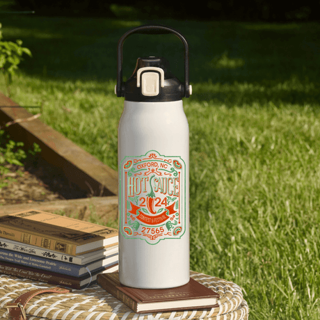 NC Hot Sauce Contest & Festival 57oz Water Bottle with vintage label design on table outdoors.