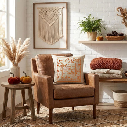 Natural linen throw pillow with a burnt orange "Fall Is Proof That Change Can Be Beautiful" quote on a leather armchair