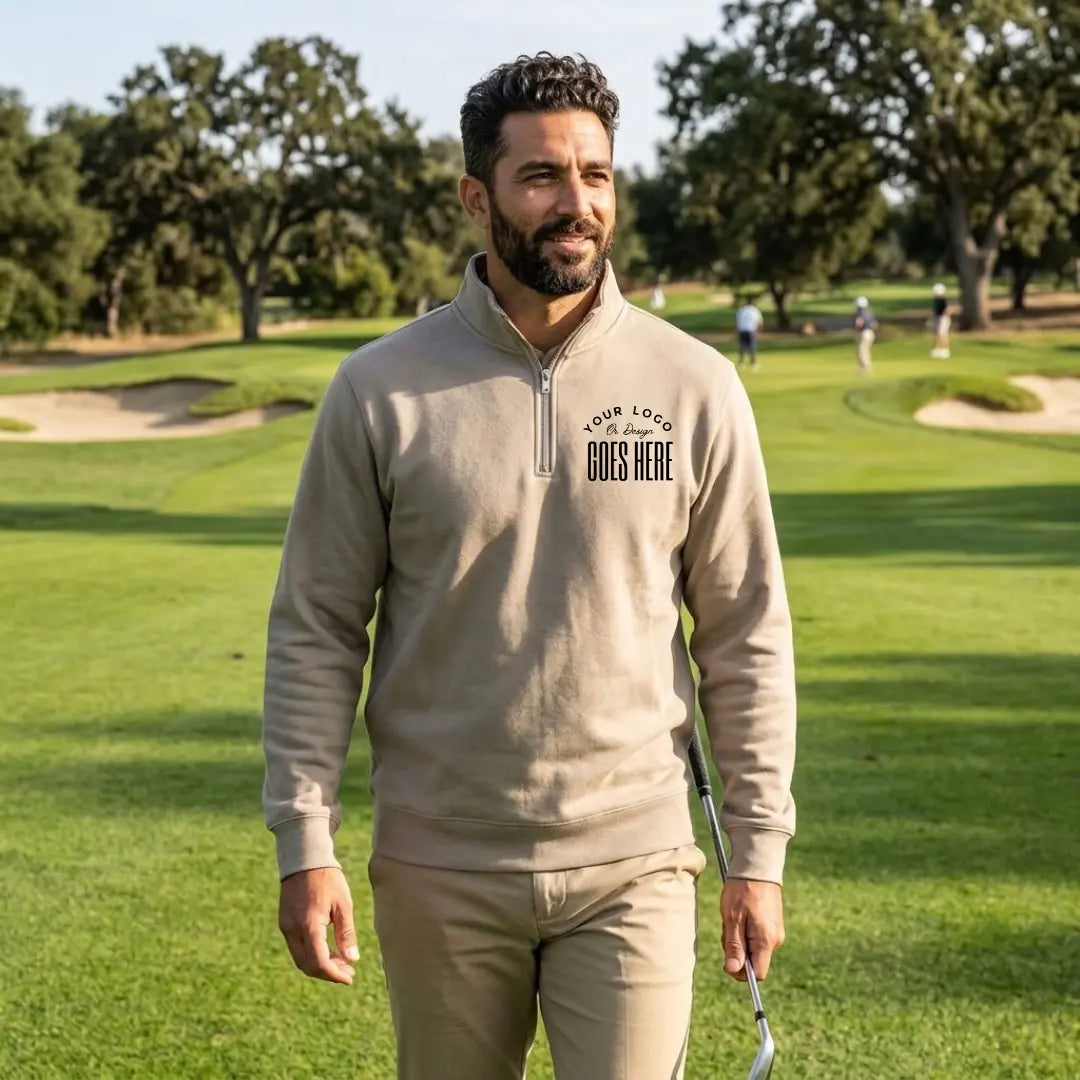 Smiling man walking a golf course in a stone gray custom quarter zip sweatshirt with a black "Your Logo or Design Goes Here" left chest placeholder