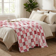 Bed with pink and white checkered blanket, pillows, and a plant in a bright bedroom.
