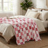 Bed with pink and white checkered blanket, pillows, and a plant in a bright bedroom.