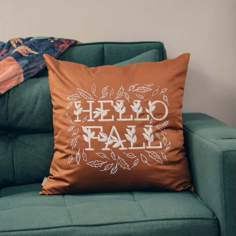 "Hello Fall Pillow on green sofa with autumn-themed design, perfect for seasonal home decor."