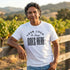 Man in a white custom t-shirt with a large black "Your Logo or Design Goes Here" center chest placeholder at a vineyard