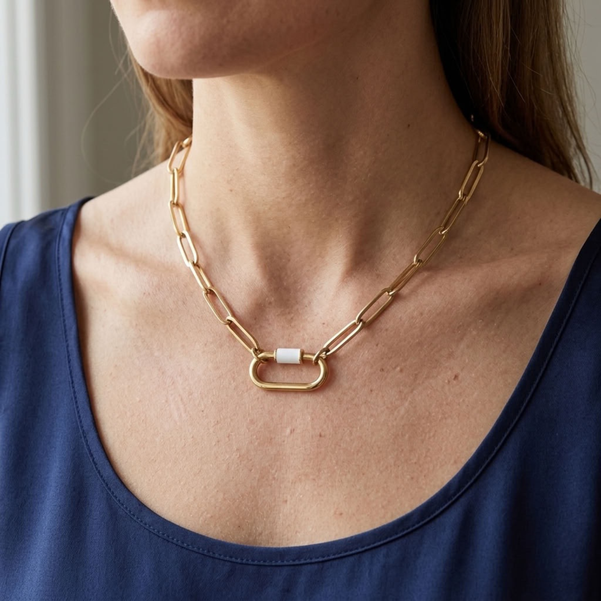 A close-up of a model wearing a gold chain necklace with a central white cylindrical accent, styled with a navy blue top.
