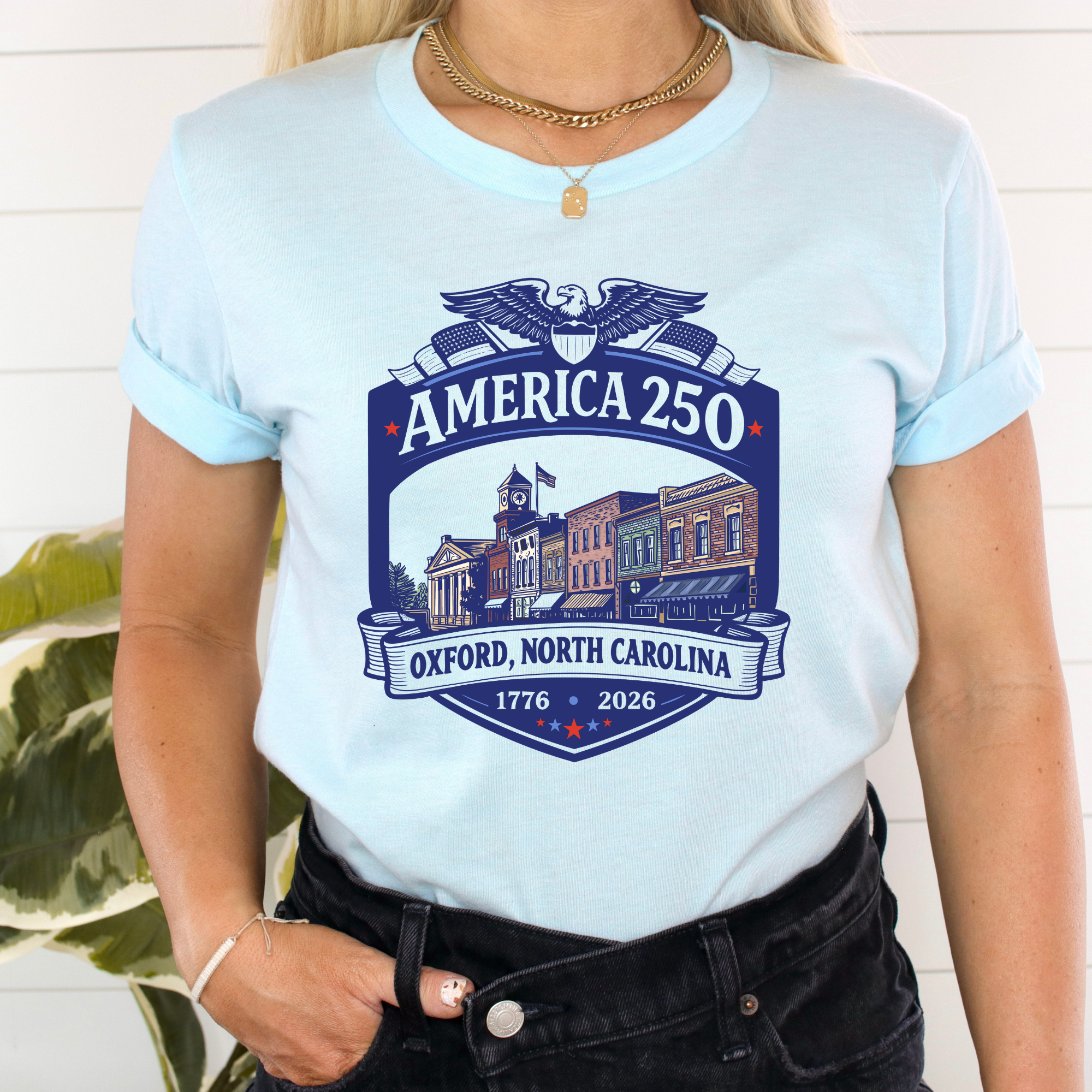 A woman wearing a light blue t-shirt with a navy blue graphic that reads &