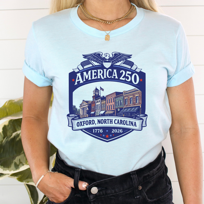 A woman wearing a light blue t-shirt with a navy blue graphic that reads &
