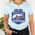 A woman wearing a light blue t-shirt with a navy blue graphic that reads &