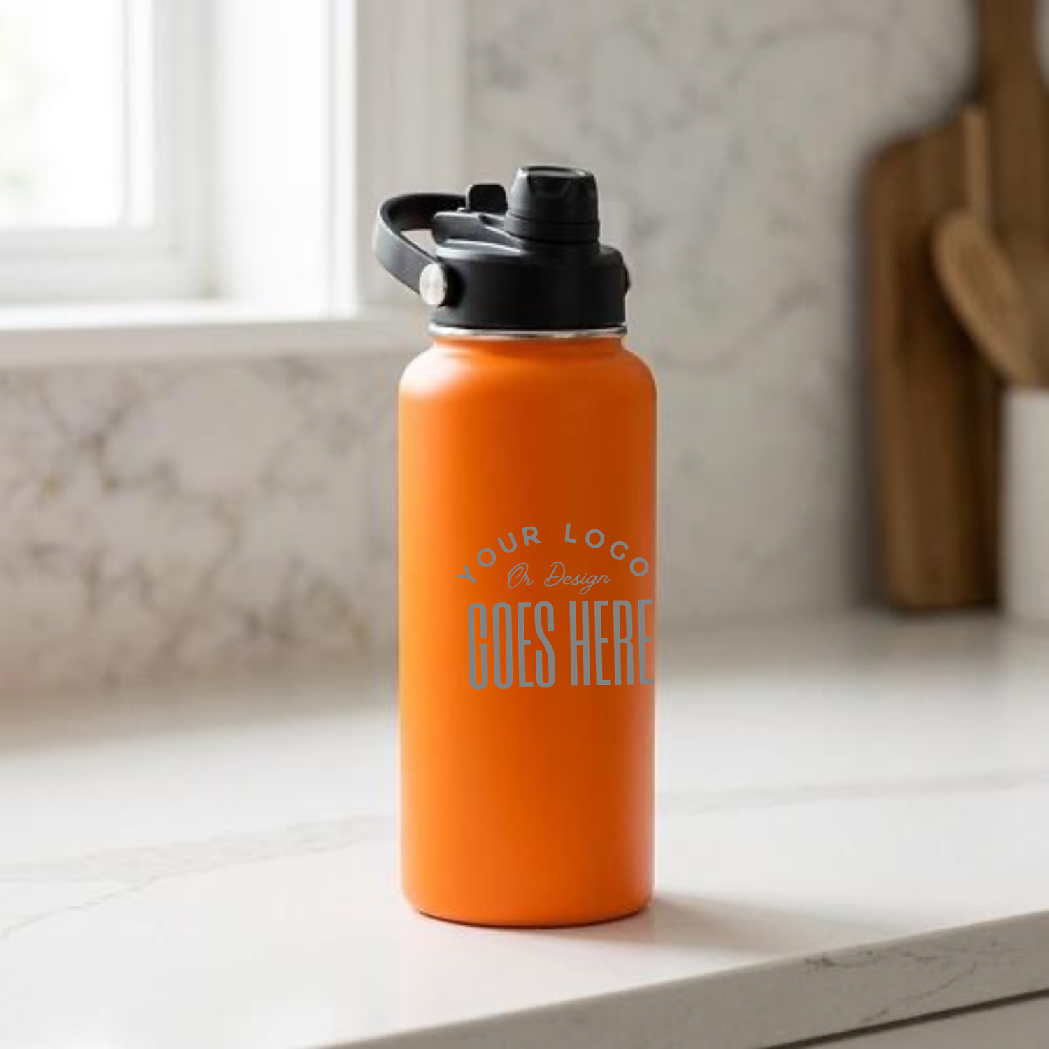 An orange insulated water bottle with a black lid sits on a white marble countertop in a kitchen setting. The bottle features a customizable graphic with the placeholder text &