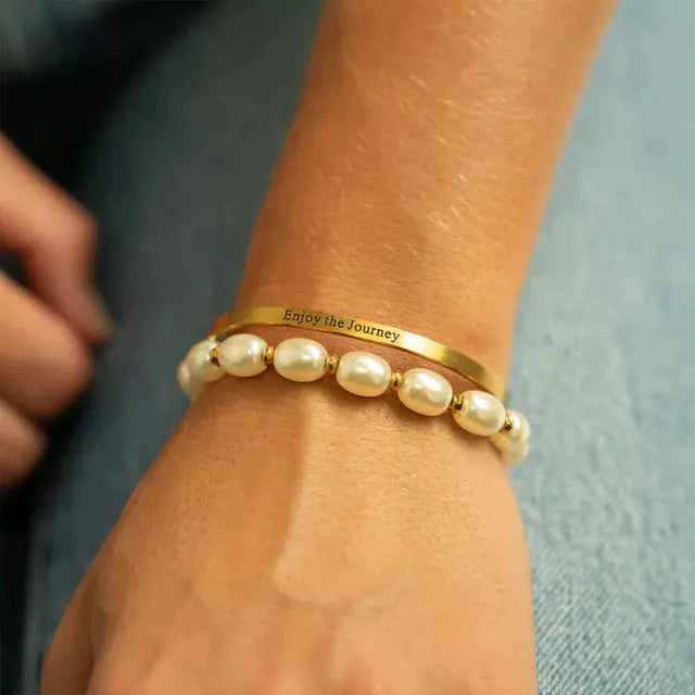 18K gold engraved bangle bracelet with "Enjoy the Journey" inscription from Winks Design Studio, LLC, shown on a model.