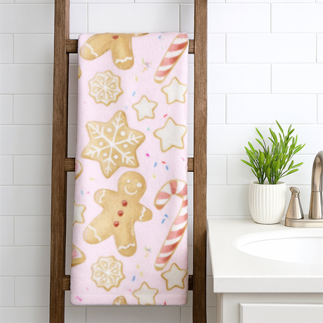 Towel with gingerbread man, snowflake, and candy cane pattern hanging on a wooden towel rack in a bathroom.